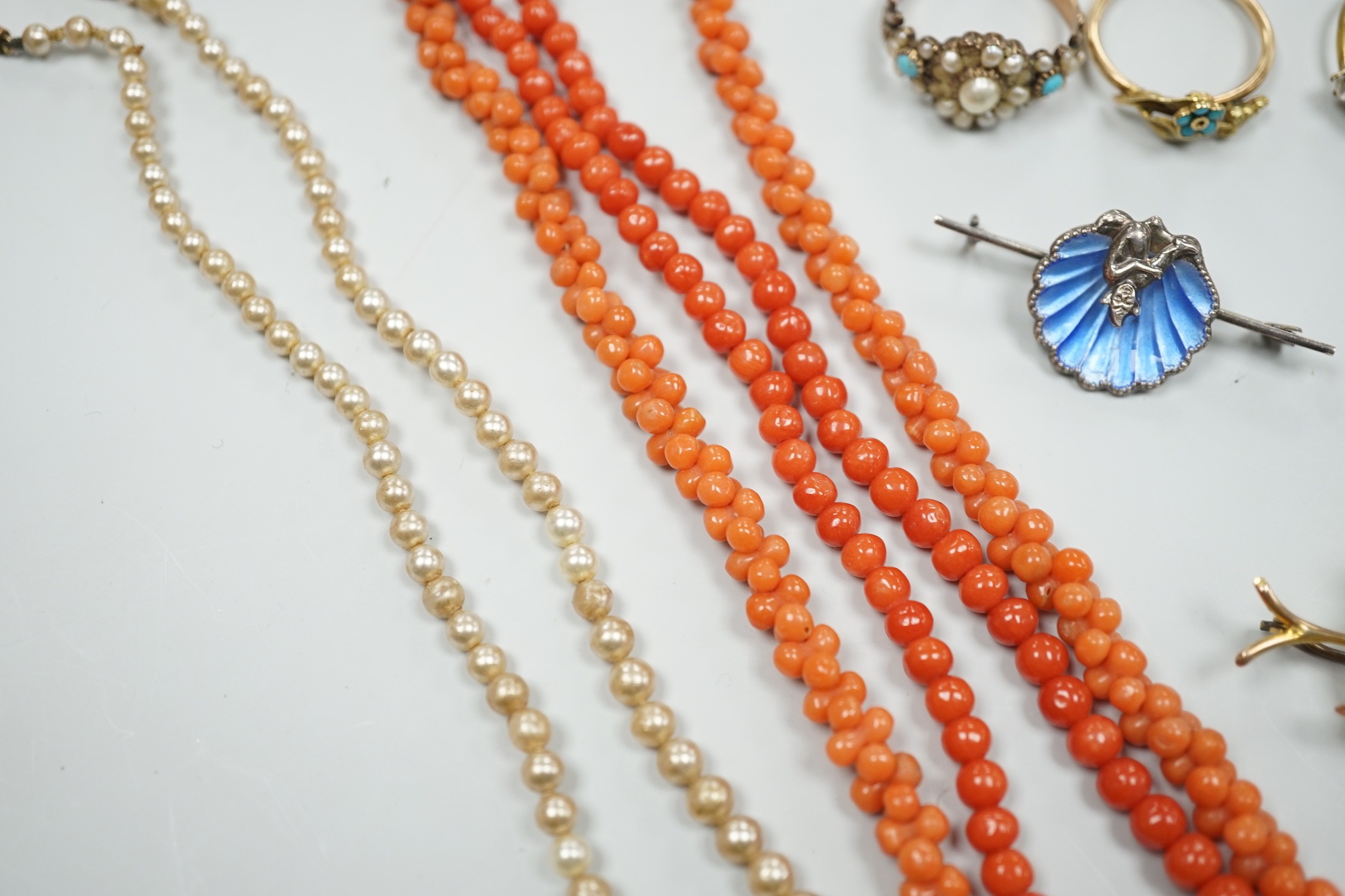 A yellow metal, seed pearl and red stone set 'bird on a branch' brooch, width 30mm, two coral bead necklaces, an enamelled white metal imp and shell brooch, three rings, a marcasite brooch and a simulated pearl necklace.